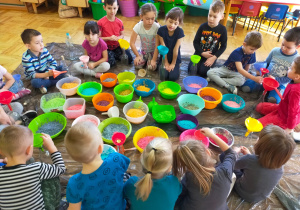 dzieci sypią do butelek kolorowy ryż przez lejki