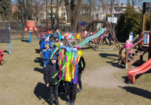 korowód przedszkolaków z Marzanną maszeruje po ogrodzie obok zjeżdżalni