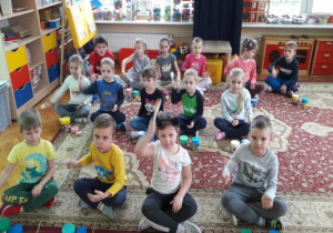 dzieci siedzą na dywanie, w rzędach i grają na grzechotkach z łyżek