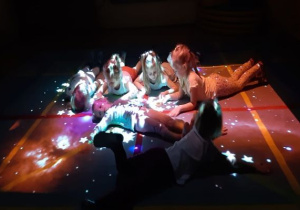 ciemno, dzieci leżą na macie, w świetle świecącym w kształcie gwiazd z FUN FLOOR
