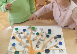 dziewczynki naklejają kapsle na plakacie jako liście na drzewie