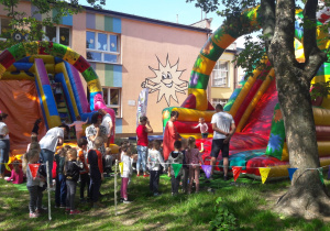 dzieci w ogrodzie przedszkolnym bawią się na dmuchanych zjeżdżalniach a część z nich czeka w kolejce