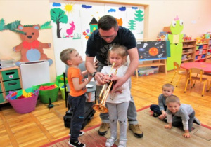 tata uczy dziewczynkę jak trzymać trąbkę a obok stoi chłopiec
