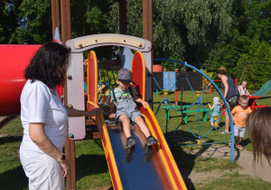 dzieci z rodzicami w ogrodzie przedszkolnym korzystają z urządzeń terenowych