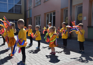 "Tęcza" - taniec grupy VII - dziewczynki ubrane w żółte koszulki i złote spódniczki a chłopcy są w ciemnych spodniach, wszyscy na nadgarstkach mają kolorowe wstążki