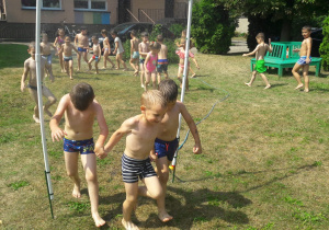 chłopcy biegną pod kurtyną wodną a inne z tyłu czekają w kolejce
