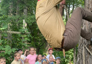 duży skrzat w czerwonej czapce wspina się po linie na drzewo