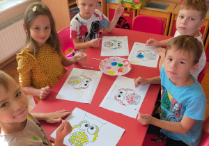 dzieci przy stoliku stemplują patyczkiem i farbą kropki na konturze sowy