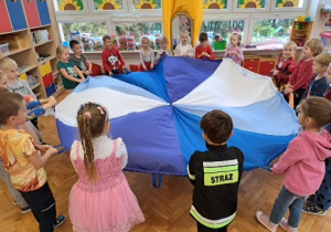 dzieci bawią się z chustą animacyjną w kolorach bieli i odcieni niebieskiego w sali