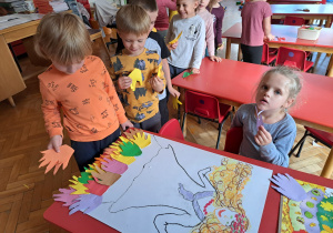 dzieci podczas wykonywania pracy "Pani Jesień" - chłopiec nakleja wyciętą dłoń na suknię pani Jesieni