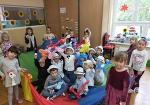 chłopcy siedzą na kolorowej chuście , w białych kapeluszach i trzymają balonowe pieski