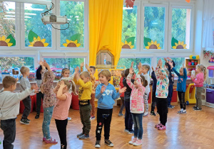 dzieci tańczą w parach w sali i klaszczą w dłonie nad głowami