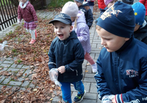 przedszkolaki idą po chdniku z założonymi jednorazowymi rękawiczkami i szukają śmieci