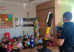 dzieci słuchają strażnika miejskiego, który pokazuje sygnalizator świetlny