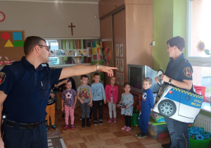 dzieci obserwują w jaki sposób powinny poruszać się pojazdy na drodze w wykonaniu funkcjonariusza i funkcjonariuszki Straży Miejskiej