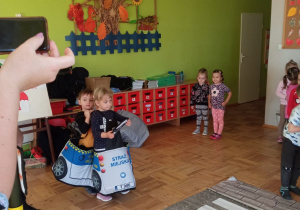 dzieci bawią się w ruch uliczny - chłopcy w wozie straży miejskiej stoją przed pasami rozłożonymi na podłodze