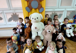 zdjęcie przedszkolaków z grupy II z maskotkami misiów i dwoma dużymi plusakami misiów