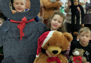 dziecko pozuje w foto budce - miś a wokół koledzy i koleżanki z pluszakami
