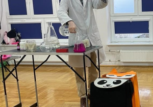 chemik wlewa przezroczysty płyn do menzurki z różowym płynem a w drugiej dłoni trzyma słoik z płynem w kolorze herbaty