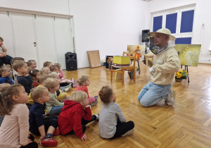 pszczelarz klęczy i pokazuje dzieciom kratkę do ula