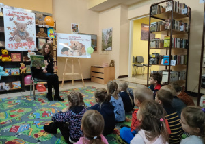 w bibliotece - dzieci siedzą i słuchają opowiadania czytanego przez panią bibliotekarkę