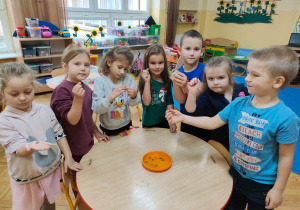 dzieci stoją wokół stolika i trzymaja i wrzucają monety do talerzyka z wodą
