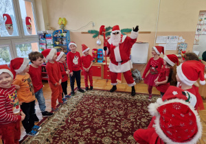 Mikołaj stoi z dziećmi w kole i macha ręką