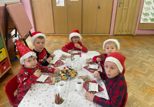chłopcy w czerwonych czapkach siedzą przy stoliku i jedzą słodkie przysmaki