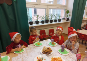 przedszkolaki w czerwonych ubraniach siedzą przy stolikach i częstują się słodkościami