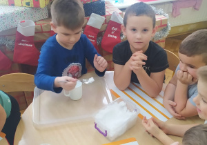 dzieci obserwują jak kolega przekłada łyżką śnieg z pojemnika do szklanki