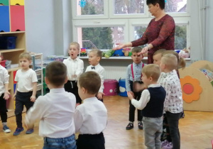 auczycielką stoją w kole, śpiewają i pokazują dłonie
