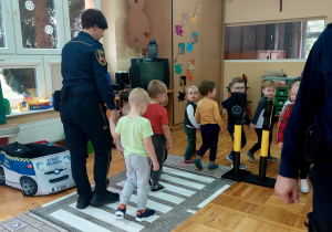 dzieci wraz ze strażniczką przechodzą parami po pasach w sali
