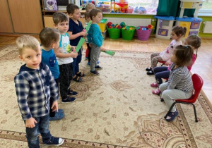 chłopcy stoją i składają życzenia a dziewczynki siedzą na krzesełkach