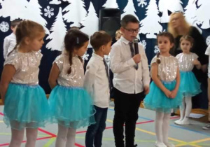 dzieci ustawione w szeregu recytują wiersz podczas występu dla babci i dziadka