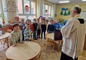 ksiądz rozmawia z dziećmi w sali