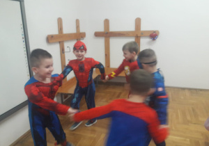 chłopcy w kostiumach super bohaterów tańczą w kole trzymając się za dłonie