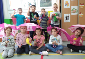 dziewczynki siedzą pod parasolkami a chłopcy stoją za nimi i trzymają wykonane przez siebie parasolki