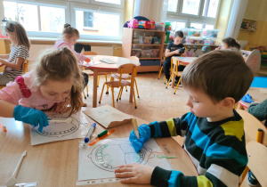 dzieci rysują zarazki na zębach na kartce z wydrukowaną szczęką i oglądają je w lusterku