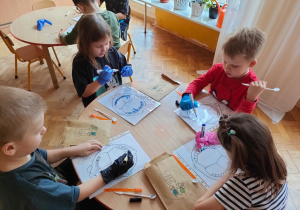 dzieci rysują kolorowymi mazakami zarazki na zębach na kartce z wydrukowaną szczęką