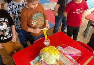 dzieci przygotowują Marzannę - chłopcy przyklejają włosy kukły
