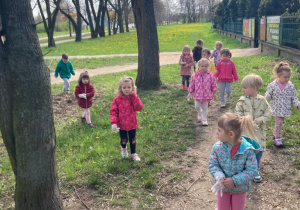 przedszkolaki w jednorazowych rękawiczkach zbierają śmieci wokół ogrodzenia przedszkolnego