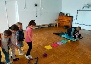 przedszkolaki stoją przed ścieżką z kolorowych, kwadratowych klocków, która prowadzi do pieska
