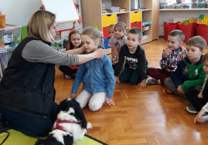 dzieci przyglądają się pieskowi Molly siedzącemu na macie