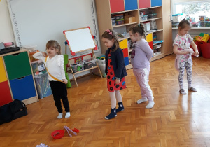 dziewczynki stoją przy karmie dla psa i przed kolorowymi, kwadratowymi matami