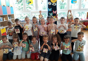 przedszkolaki z grupy VI z obrazkami na ścianę z naklejonymi drewnianymi patyczkami w formie ramki i kolorowymi kwiatkami oraz serduszkami
