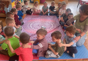 przedszkolaki siedzą w kole i wykonują masażyk osobie siedzącej przed nią