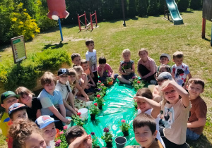 w ogrodzie dzieci z doniczkami i kwiatkami siedzą wokół maty