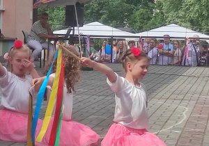 dziewczynki klęczą na tarasie z uniesionymi do góry patyczkami z wstążkami