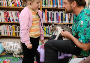 dziewczynka słucha bicia serca kota, który siedzi na kolanach pana weterynarza