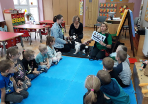 dzieci siedzą w kole wraz z instruktorkami i psami